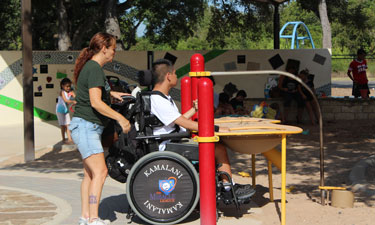 A park patron plays at the elevated sand table while others enjoy the shaded sand box and custom designed learning wall.